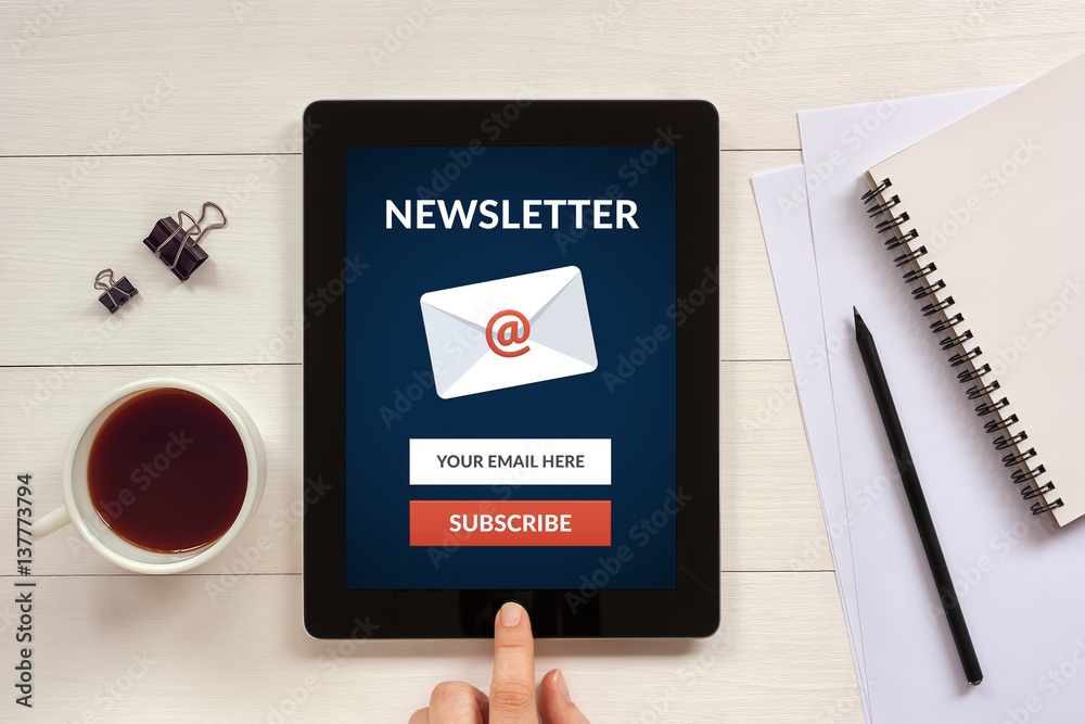 Subscribe newsletter concept on tablet screen with office objects on white wooden table. All screen content is designed by me. Flat lay